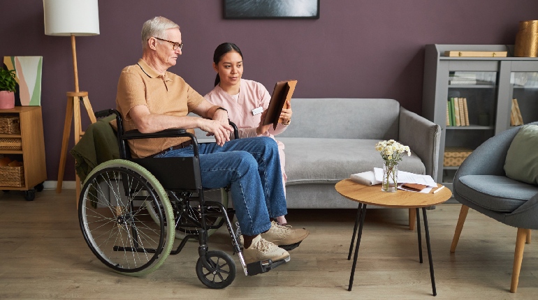 A senior man in a wheelchair comfortably reaching for a book in an accessible library, highlighting the dignity in Senior living in India with 24x7 health support