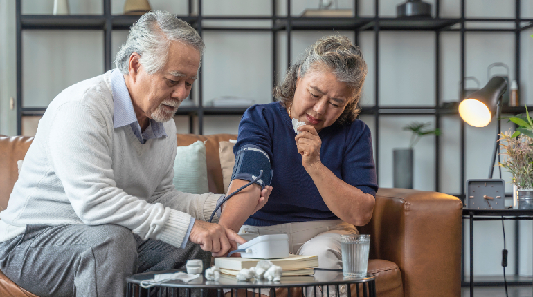 A professional nurse checking a senior resident's blood pressure using a digital monitor at a senior living in India with 24x7 health support
