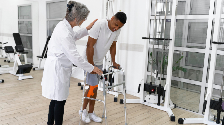 A senior resident performing guided gait exercises with parallel bars under the supervision of an orthopedic therapist at a senior care facility with round the clock healthcare in India