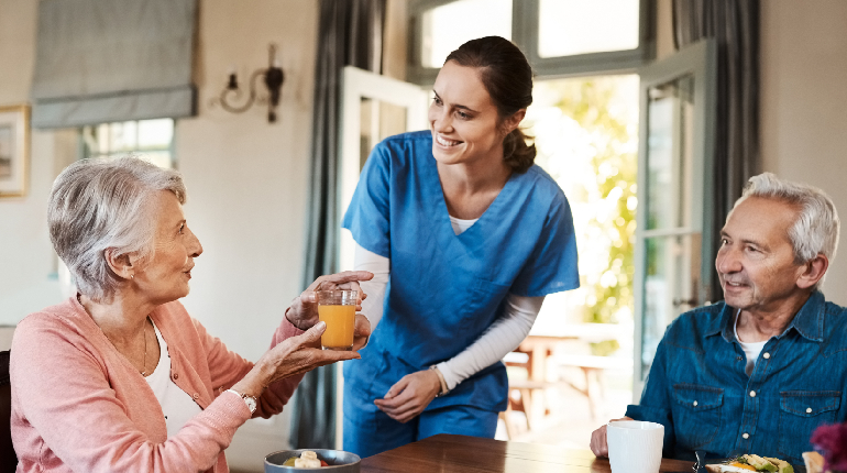 A specialized nurse offering a refreshing hydration drink to a senior resident at a residential facility for elders with 24x7 healthcare support