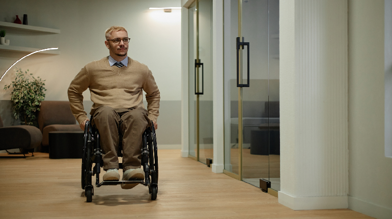 A senior resident utilizing a modern ergonomic wheelchair independently along a wide, zero-barrier corridor